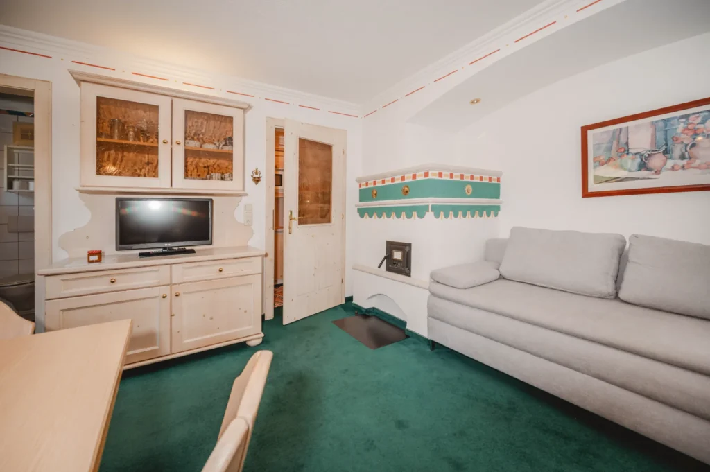 Wohnraum mit Ausziehcouch, TV und Kachelofen im Appartement Plattenkogel – Edenlehengut in Krimml